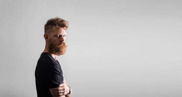 Eric Bandholz with an orange power beard and standing in front of a grey backdrop. 