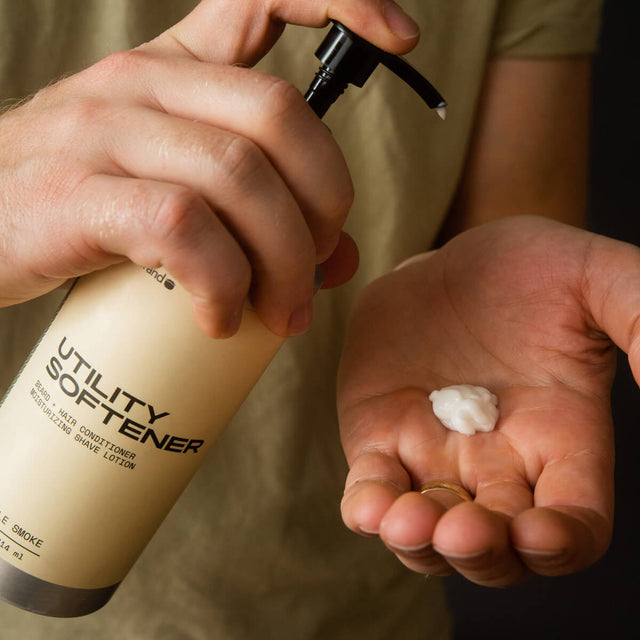 A person squeezes a pump bottle with one hand, dispensing white Utility Softener into the palm of their other hand. 