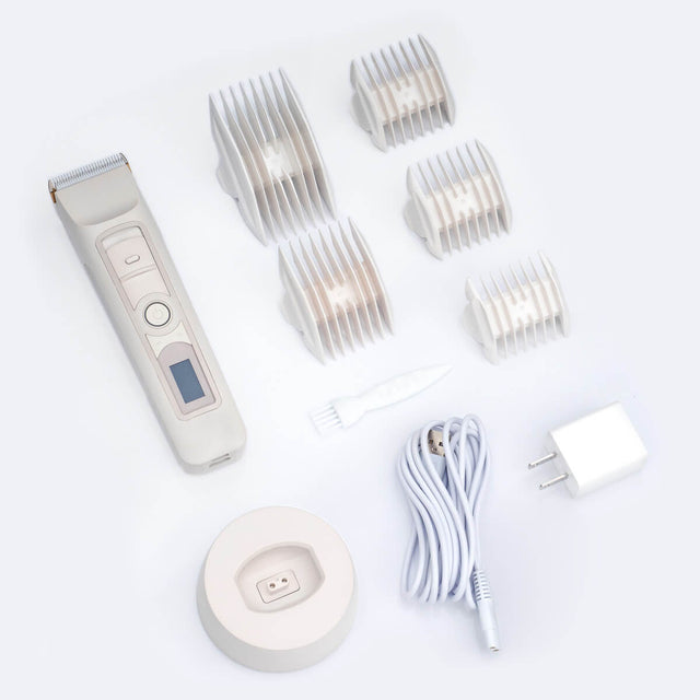 A product layout of the Beardbrand Utility Trimmer set. The image shows the main trimmer unit, five different sized attachment guards, a charging base, and a power adapter. All items are matching the minimalist aesthetic of the trimmer.