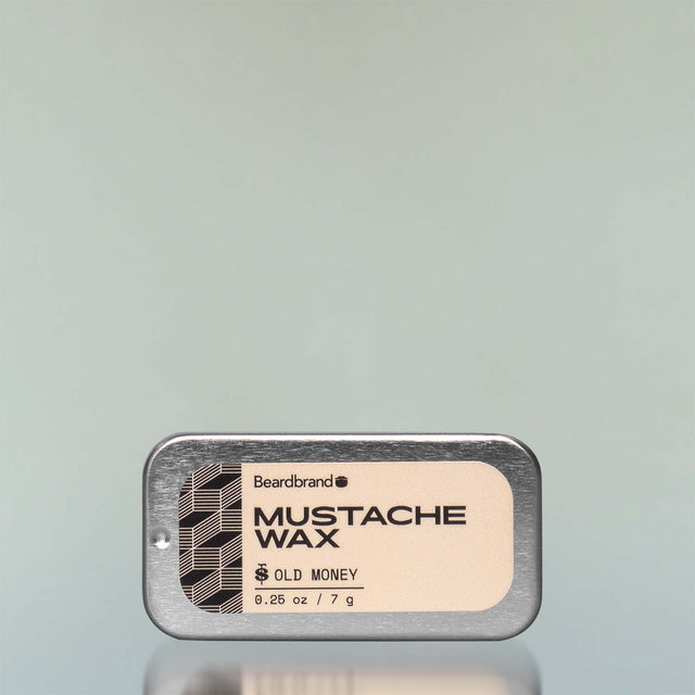 An Old Money Mustache Wax in an aluminum slide-open tray against a grey background.