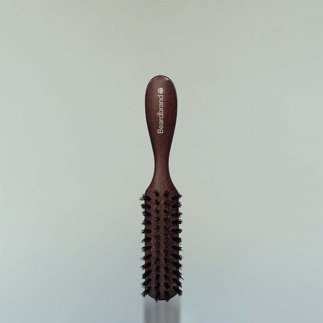 A Beardbrand 100% Boar’s Hair Travel Brush against a grey background.